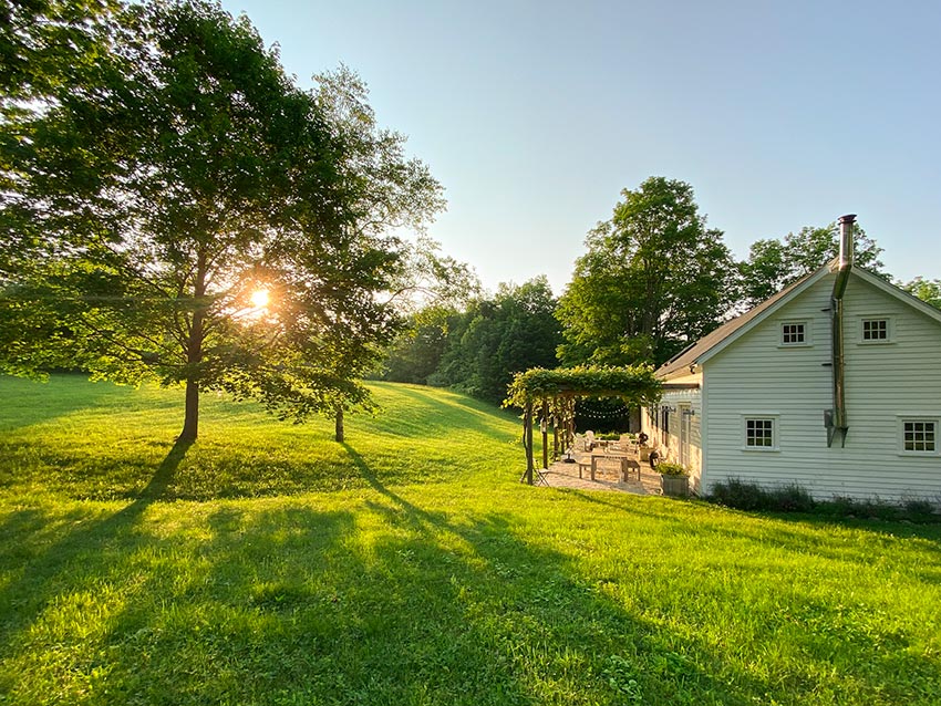 Side view of house with sun setting through trees in backyard